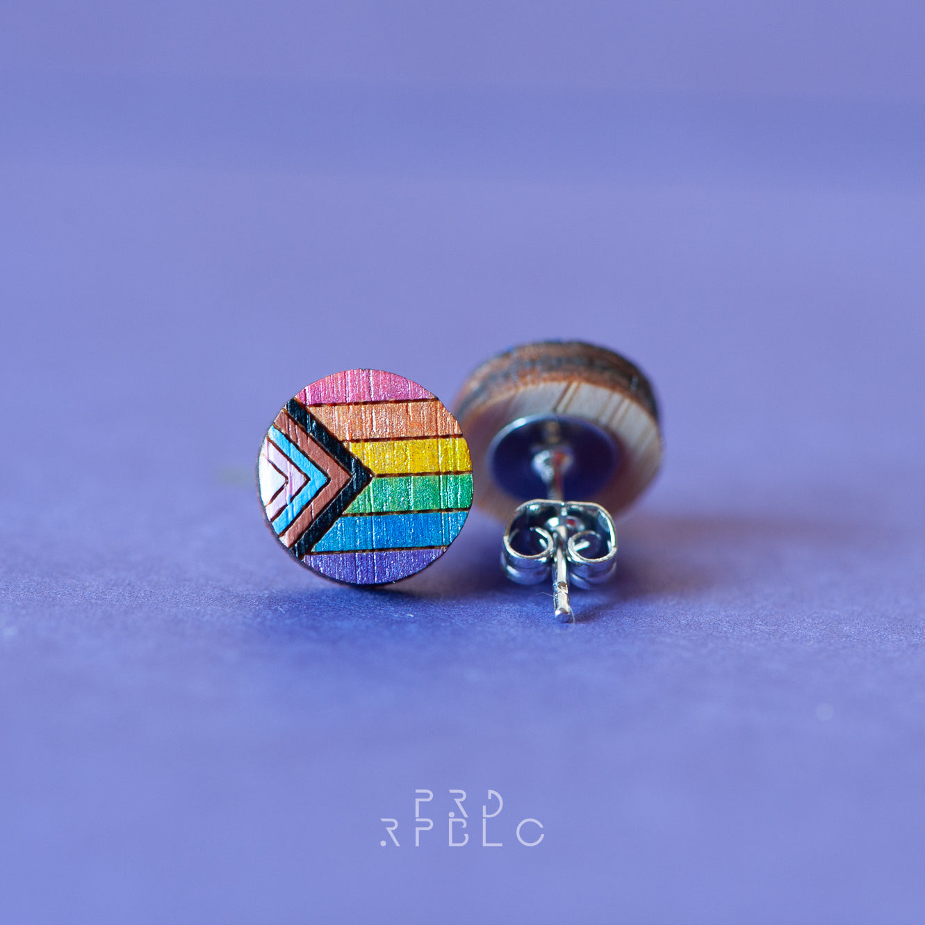 A pair of round bamboo earrings featuring a glittered Progress Pride flag design, showcased against a blue backdrop, displaying both the front and back sides of the earrings.