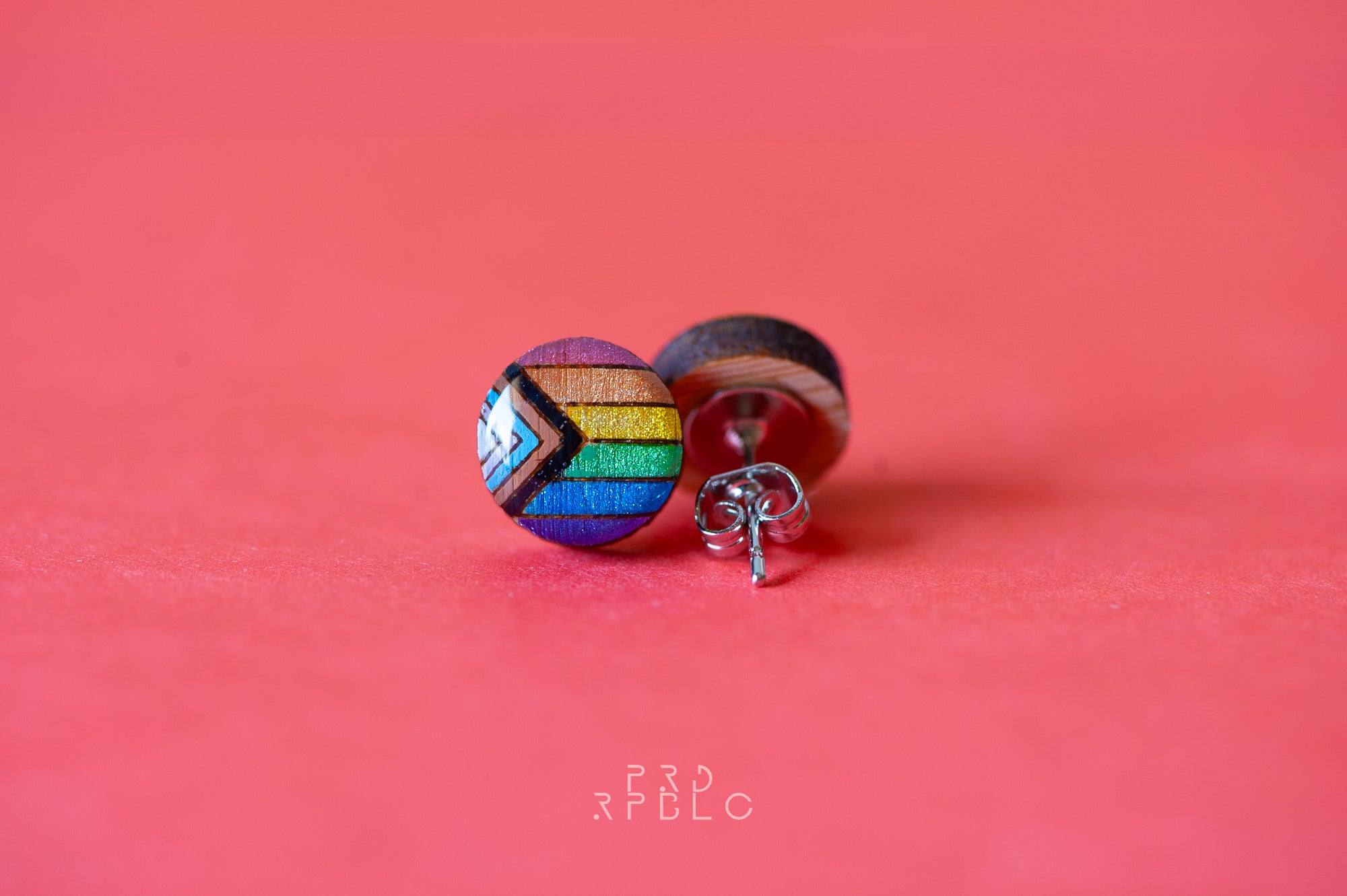 Pair of round bamboo stud earrings with a resin finish, adorned in glittering Progress Pride flag colours, set against a vibrant red backdrop, displaying both the front and back sides of the earrings.