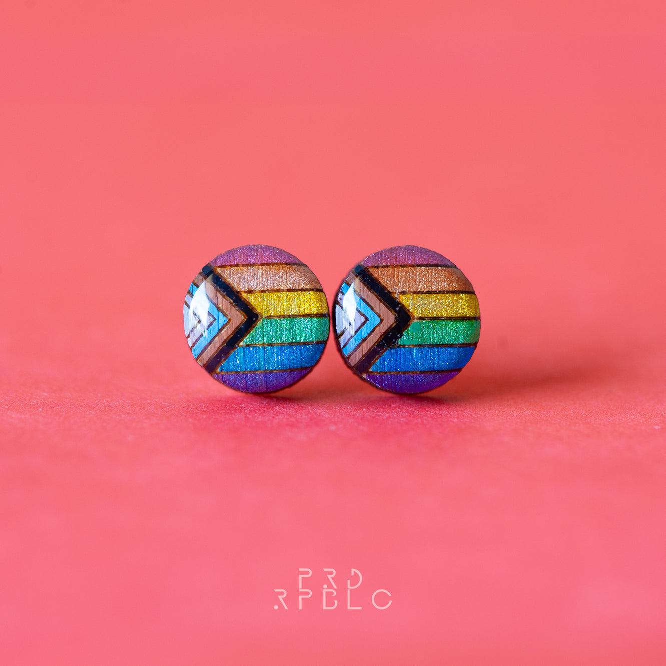Round, glitter progress pride flag bamboo stud earrings on a red backdrop