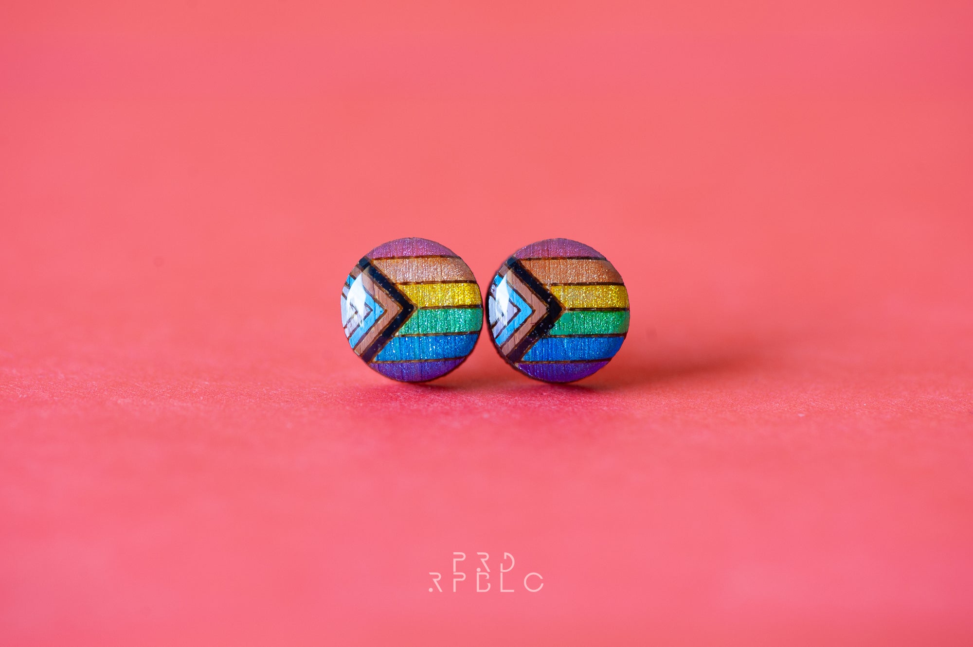 Round, glitter progress pride flag bamboo stud earrings on a red backdrop