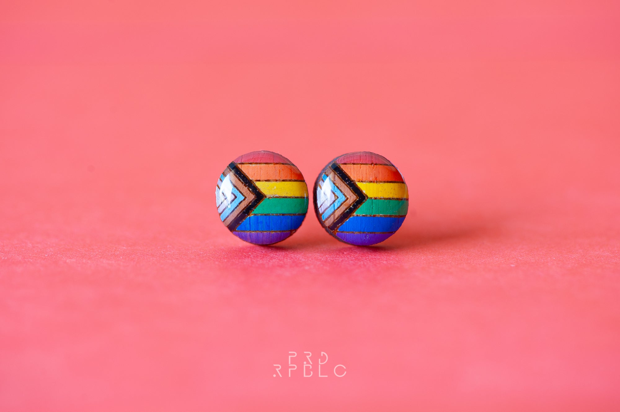 A pair of earrings featuring the progress pride flag in a geometric pattern on a red background.